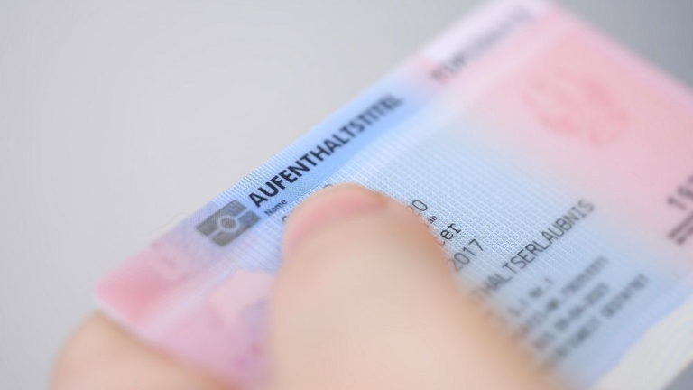 Close-up of a hand holding an Austrian residence permit card, representing the Red-White-Red Card for skilled non-EU workers.