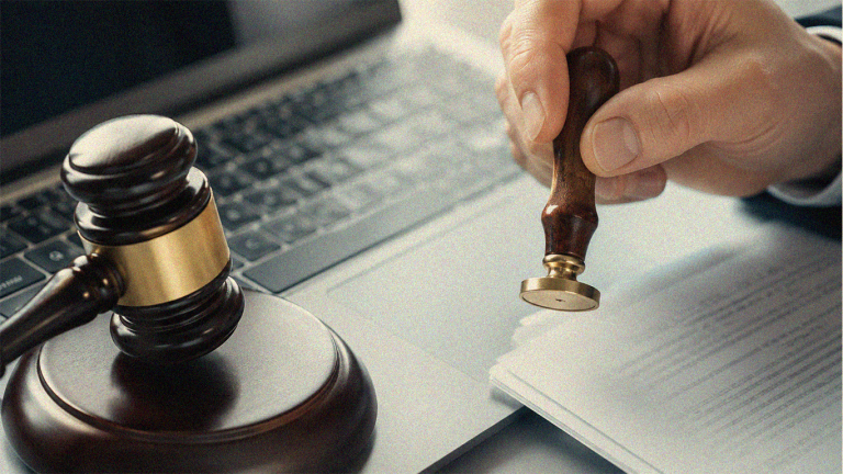 A judge's gavel and laptop beside a hand applying an official seal onto a paper document for electronic notarization.